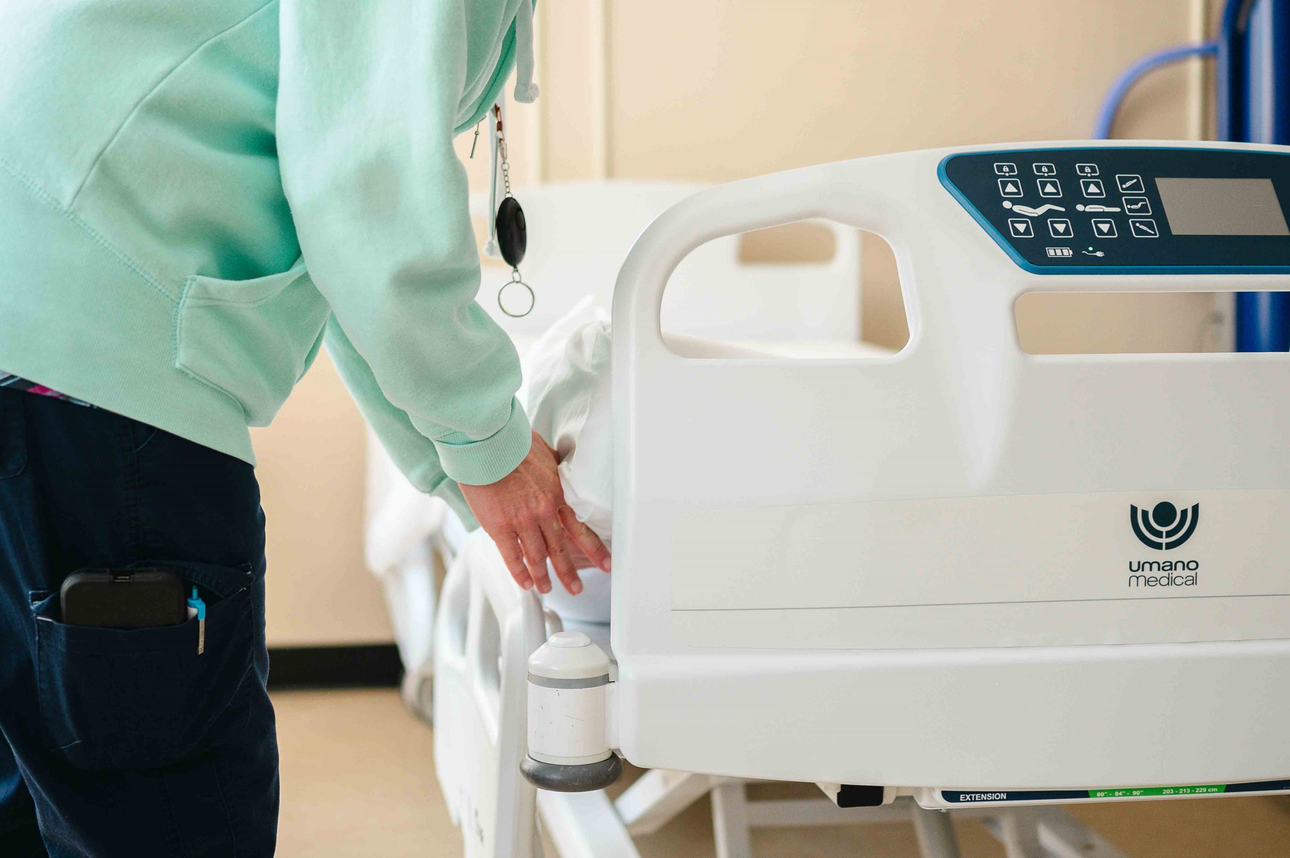 A nurse in scrubs fluffing the pillow on a patient bed.