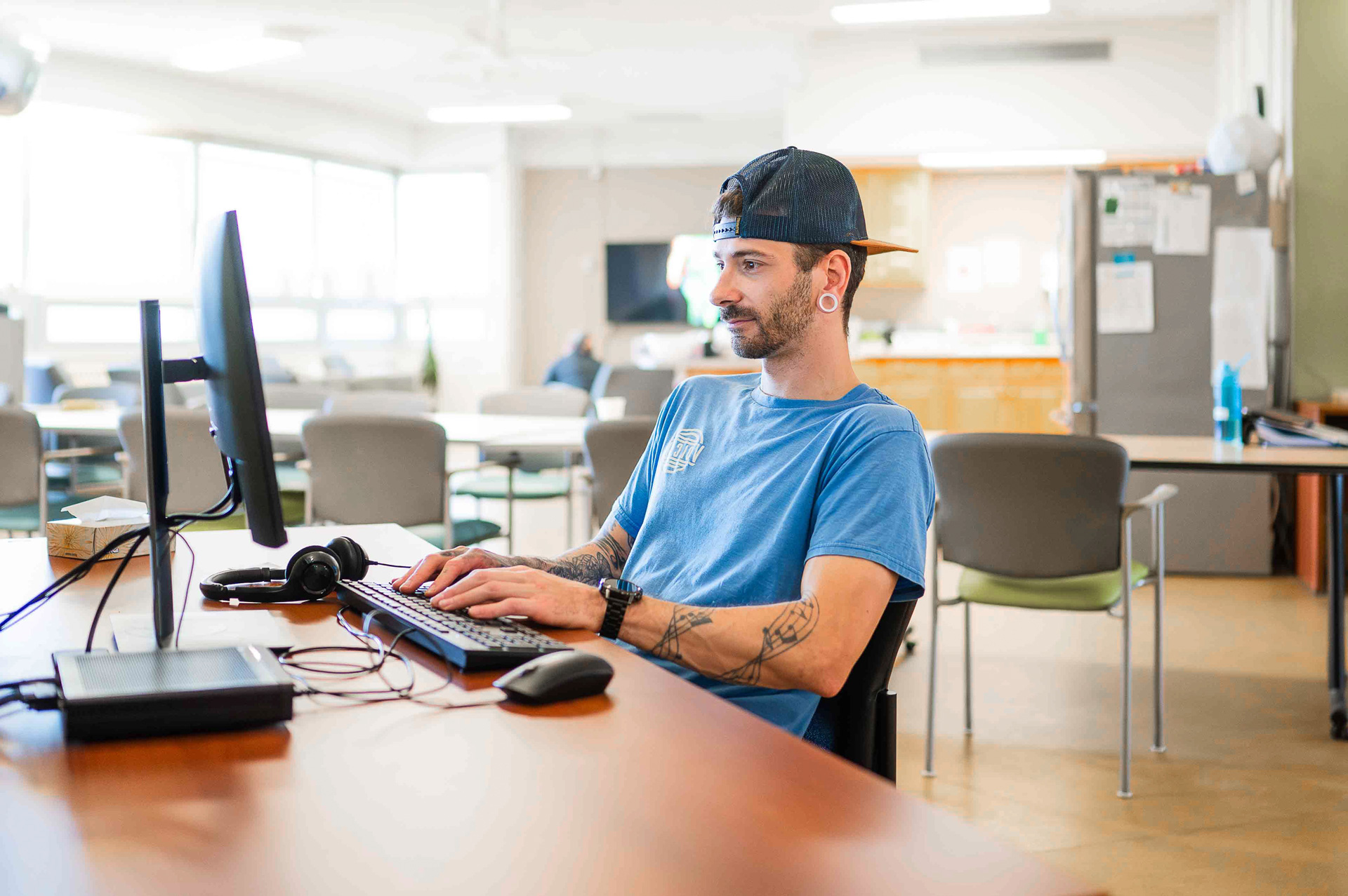 A man sitting at a table using a computer in a staff room at a mental health centre.