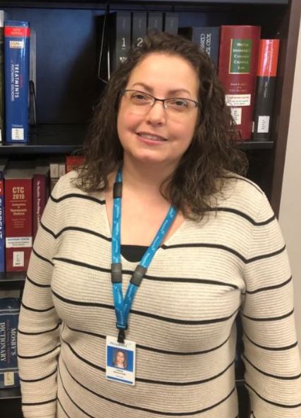 A headshot of Jolene Wintermute smiling and standing in front of book shelves.